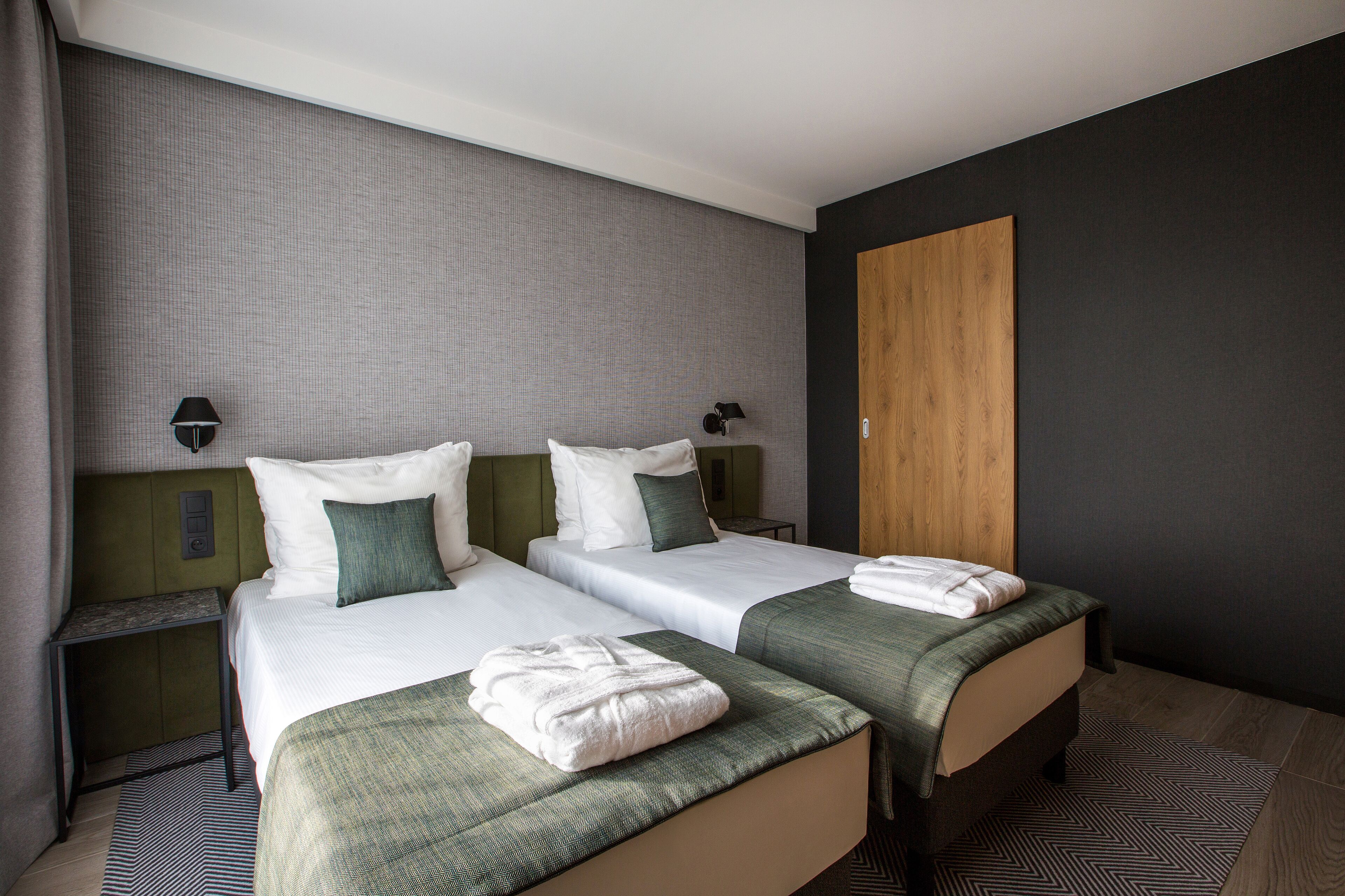 Una habitación de hotel con dos camas, un armario de madera, una mesita de noche y una lámpara de pared.