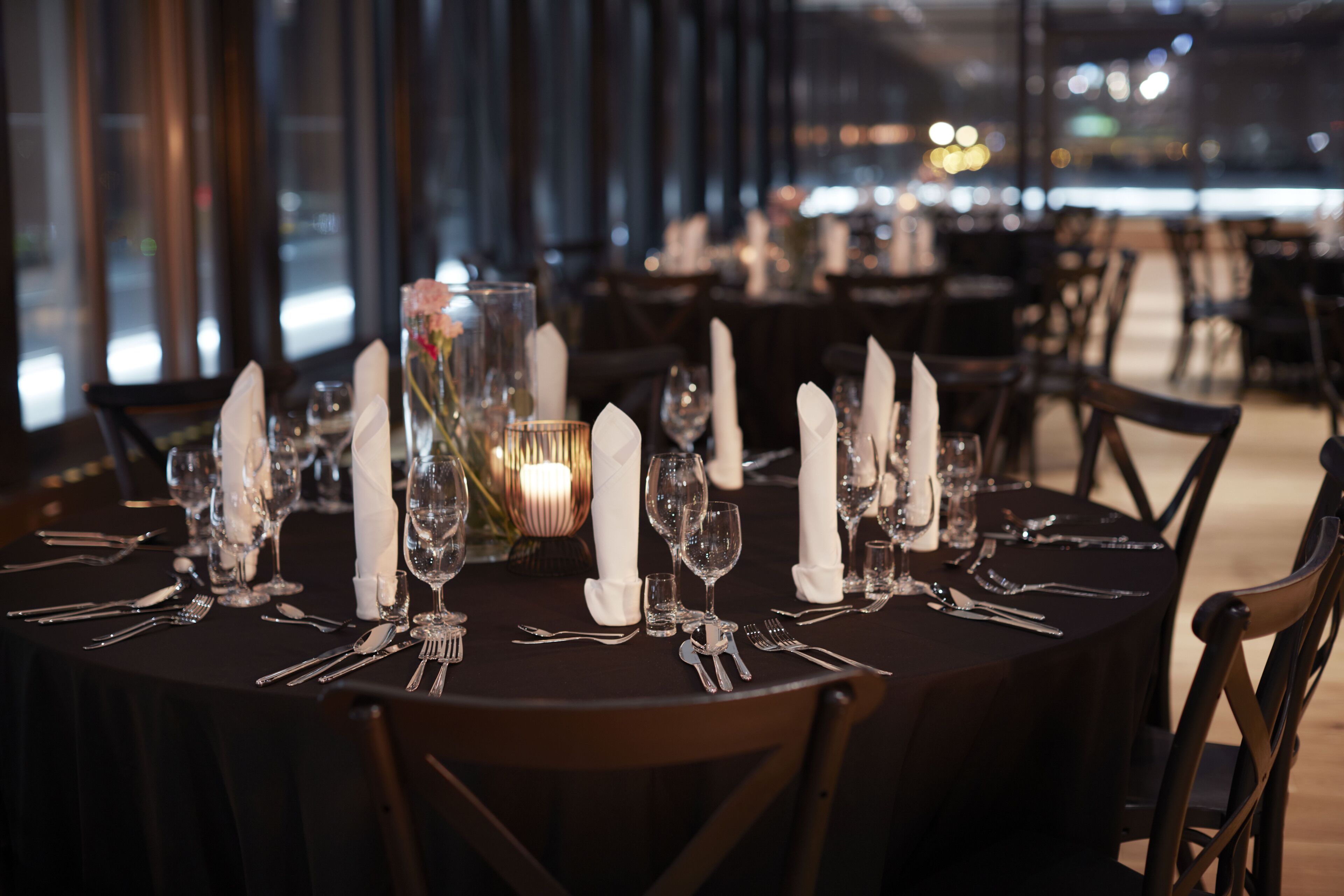 A restaurant table set with white napkins, silverware, and wine glasses, with a candle centerpiece.