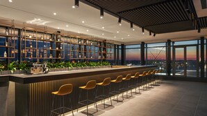 A modern bar area with a long counter, multiple shelves of bottles, and a row of yellow chairs. - Q Hotel Plus Wrocław Bielany (Kobierzyce)