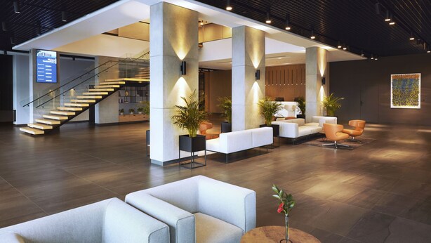 A spacious lobby with a staircase, seating areas, and a digital display. - Q Hotel Plus Wrocław Bielany (Kobierzyce)