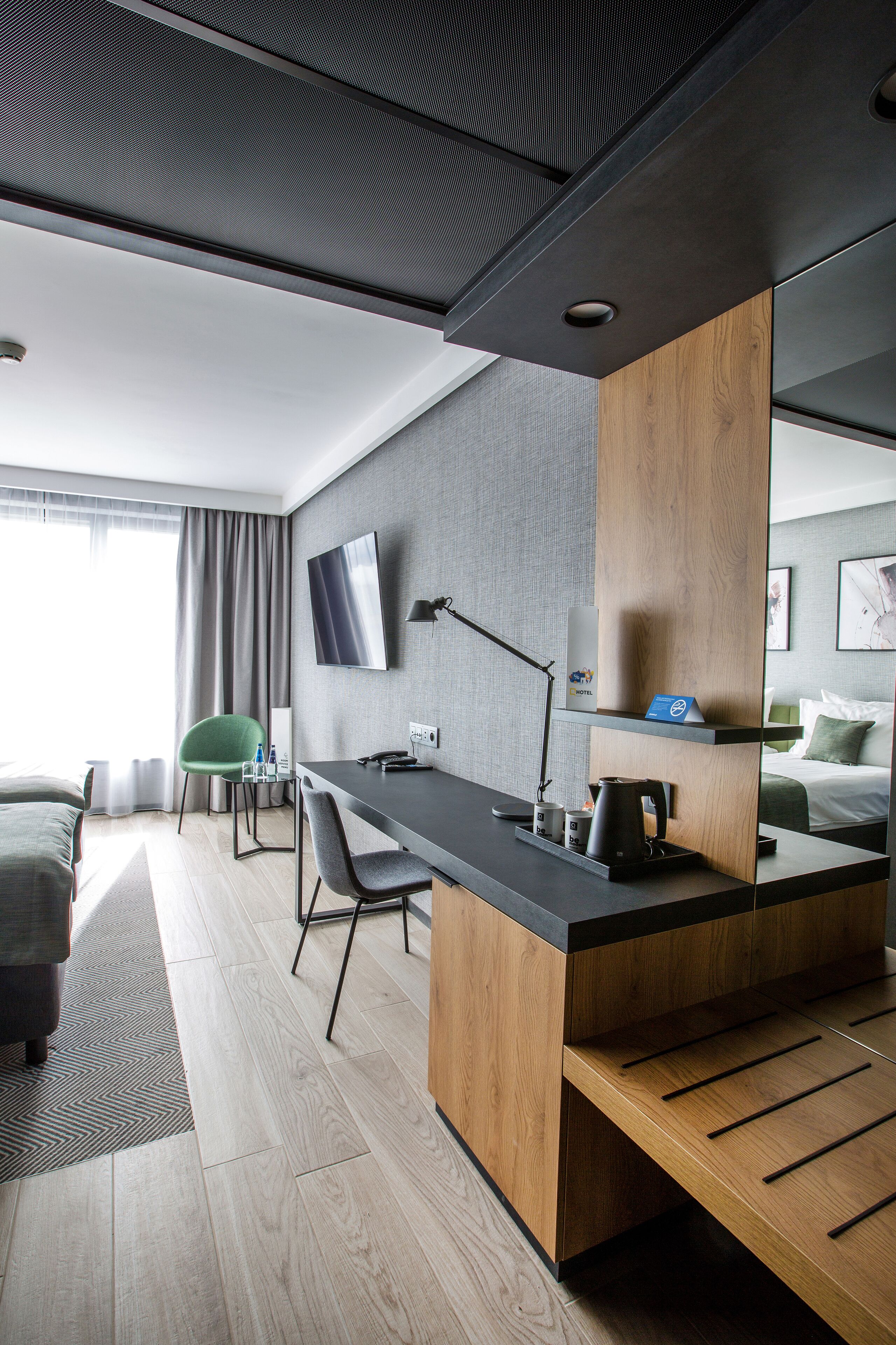 Une chambre d’hôtel moderne avec un bureau en bois, un téléviseur à écran plat, une chaise verte et un lit avec un oreiller vert.