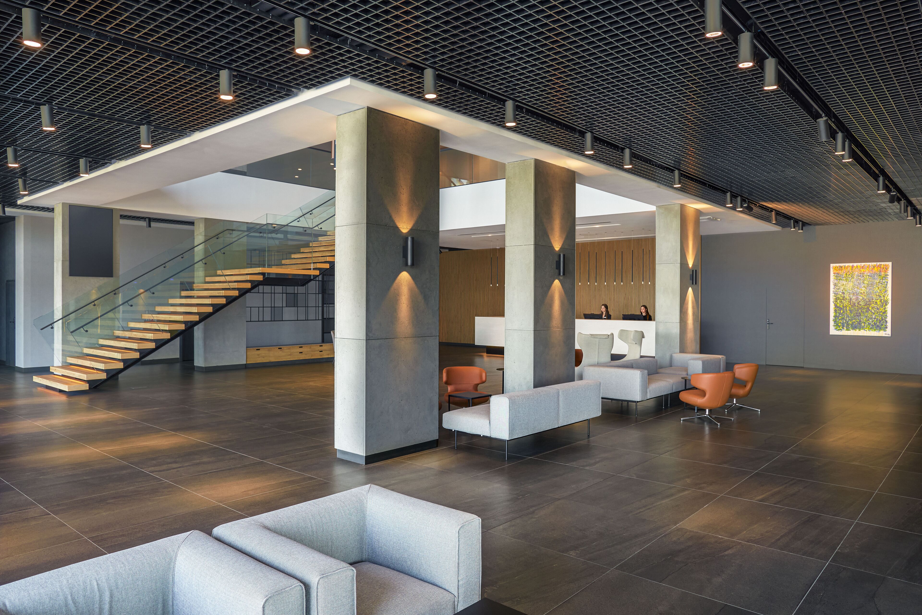 A spacious lobby with a modern design, featuring a staircase, seating areas, and a reception desk.