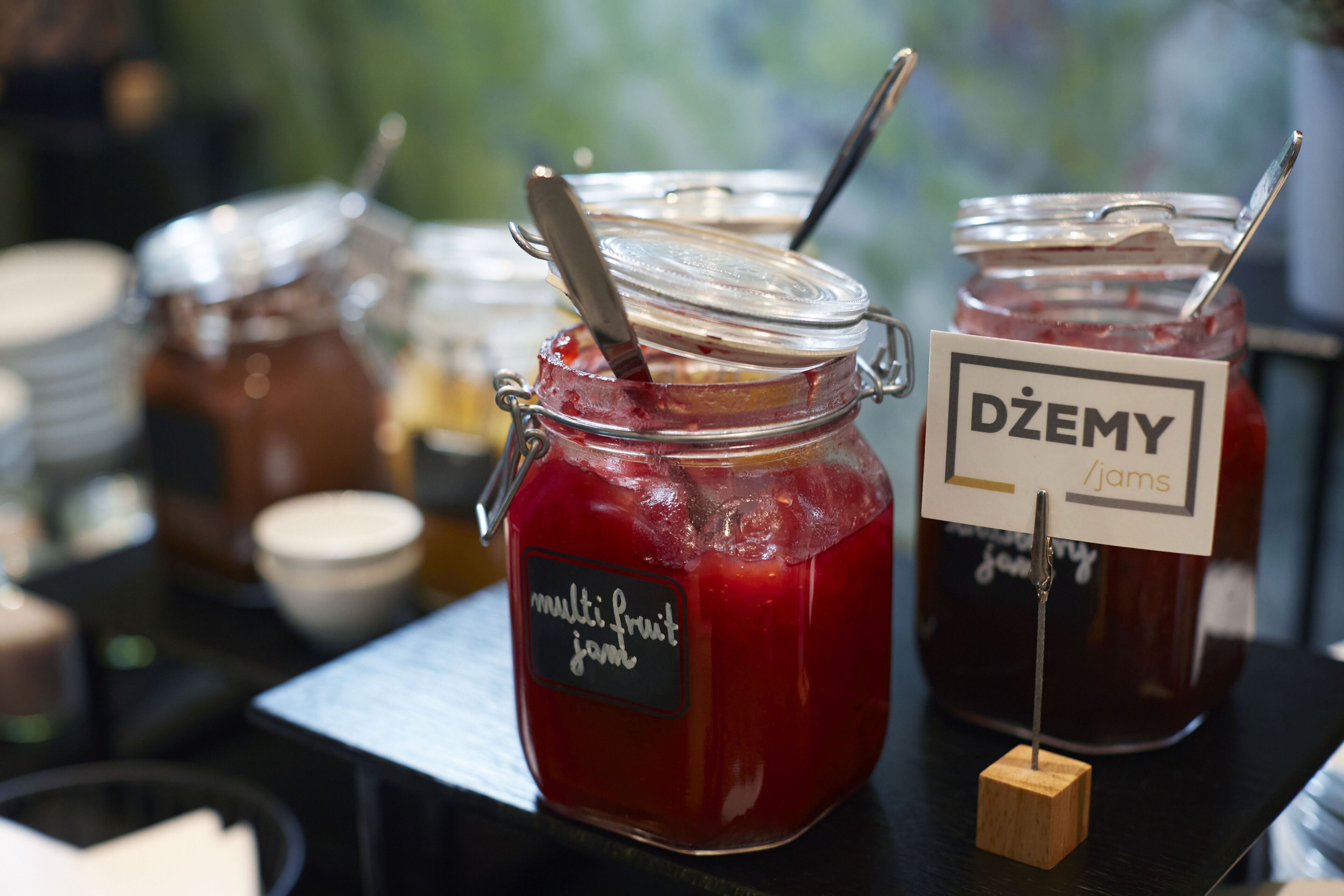 A display of multi-berry jams with labels indicating flavors like 'multi fruit jam' and 'Dźemy jams'.