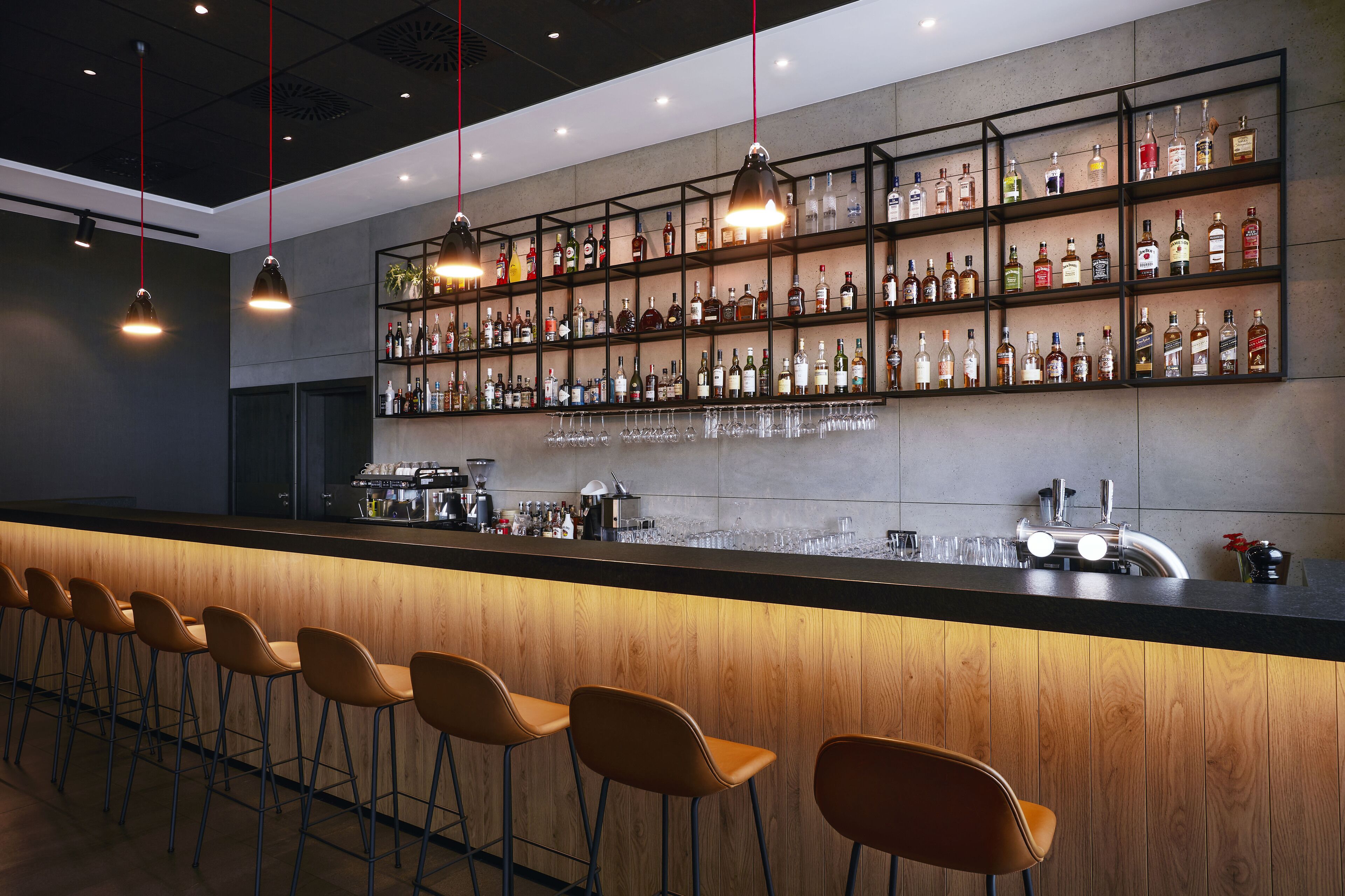 Zona de bar con una barra alargada, varios estantes llenos de botellas y algunos taburetes.