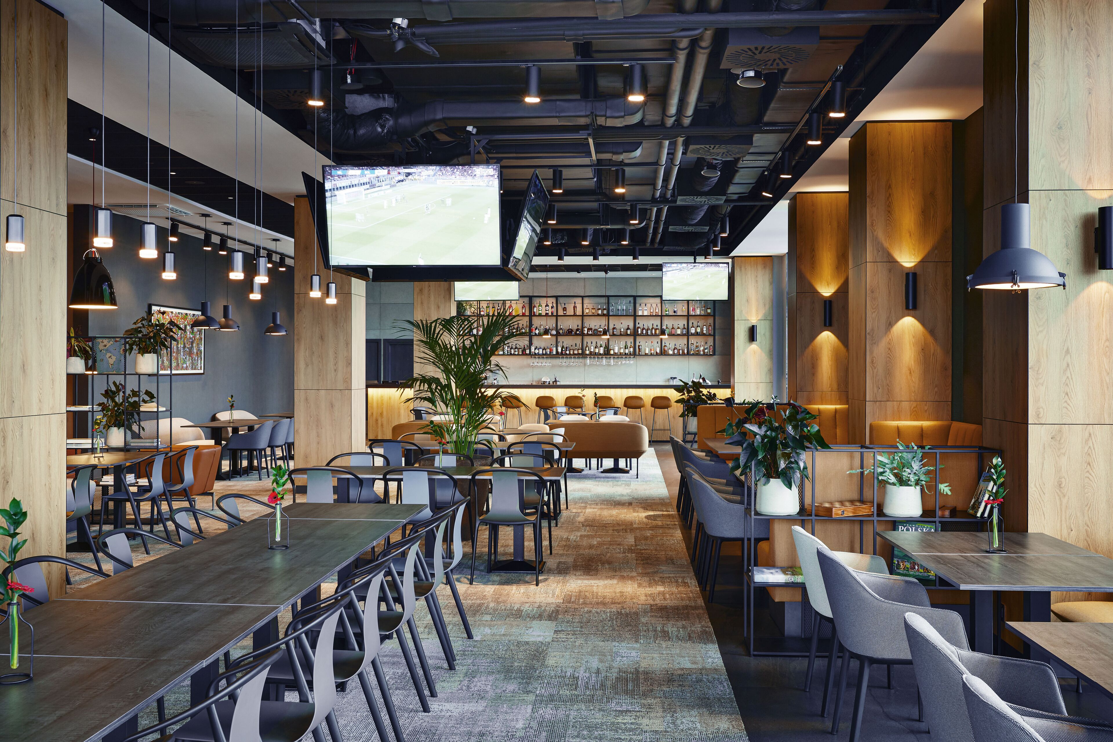 Un restaurant moderne doté d’une grande table conviviale, de plusieurs espaces de détente et d’un bar avec des étagères remplies de bouteilles.