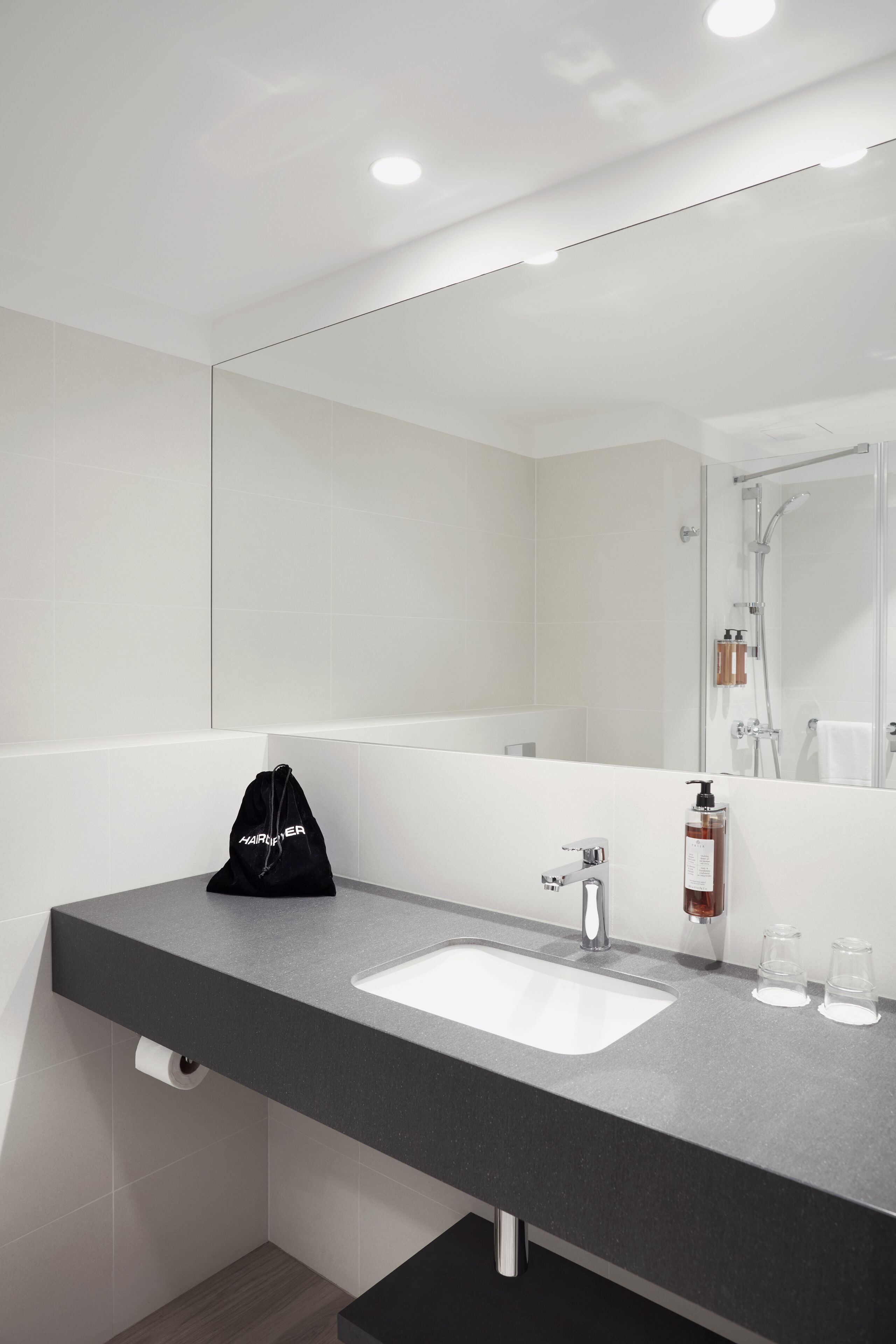 A modern bathroom with a large mirror, a sink, and a shower.