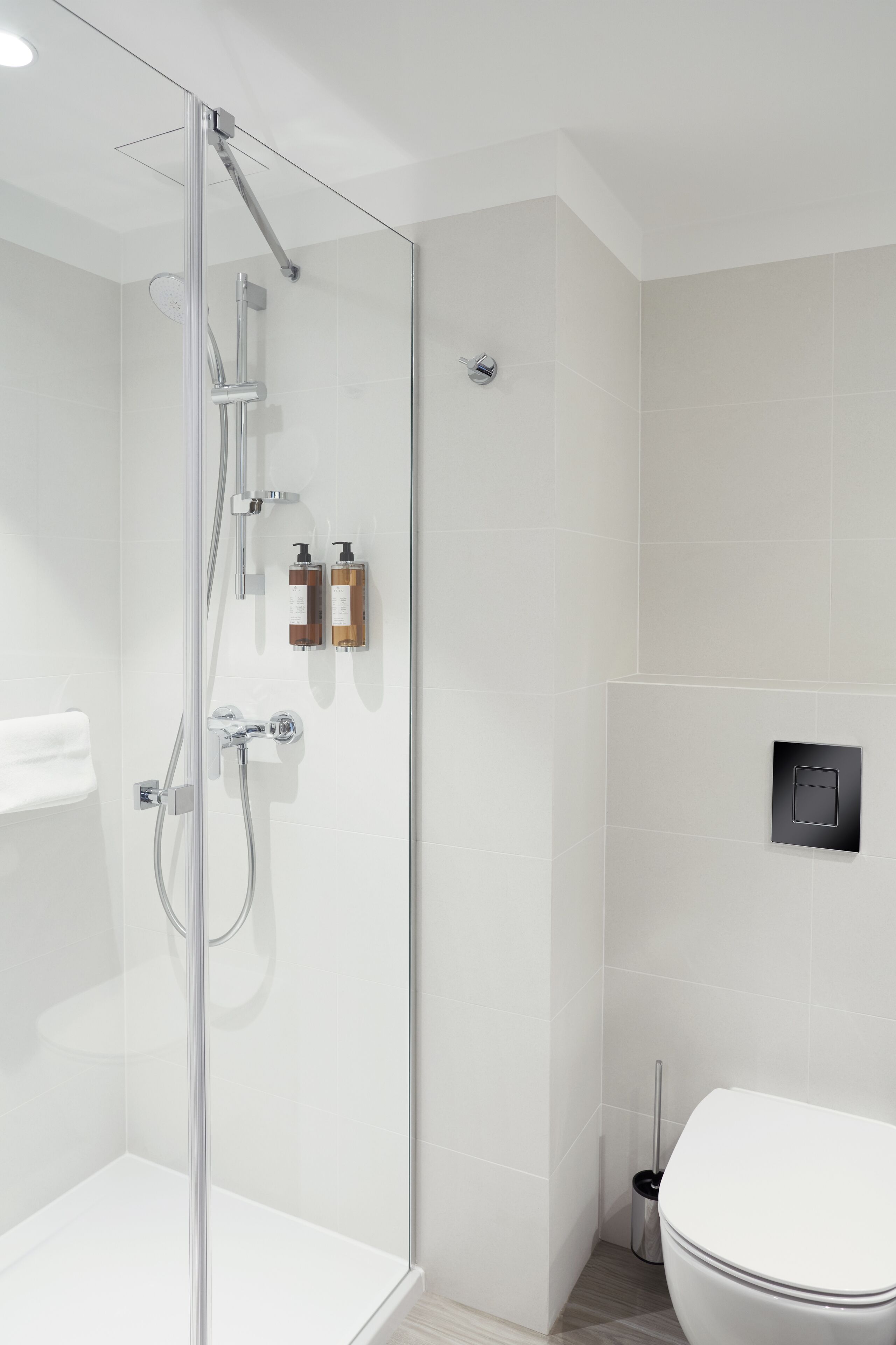 Ein modernes Badezimmer mit einer gläsernen Duschkabine, einer Toilette und einem wandmontierten Seifenspender.