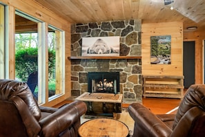 Una habitación acogedora con chimenea de piedra, sillones de cuero y un ventanal con vistas a la vegetación.