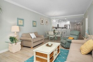 Un salon avec un canapé beige, une table basse en verre et un coin repas comprenant une table et des chaises blanches.