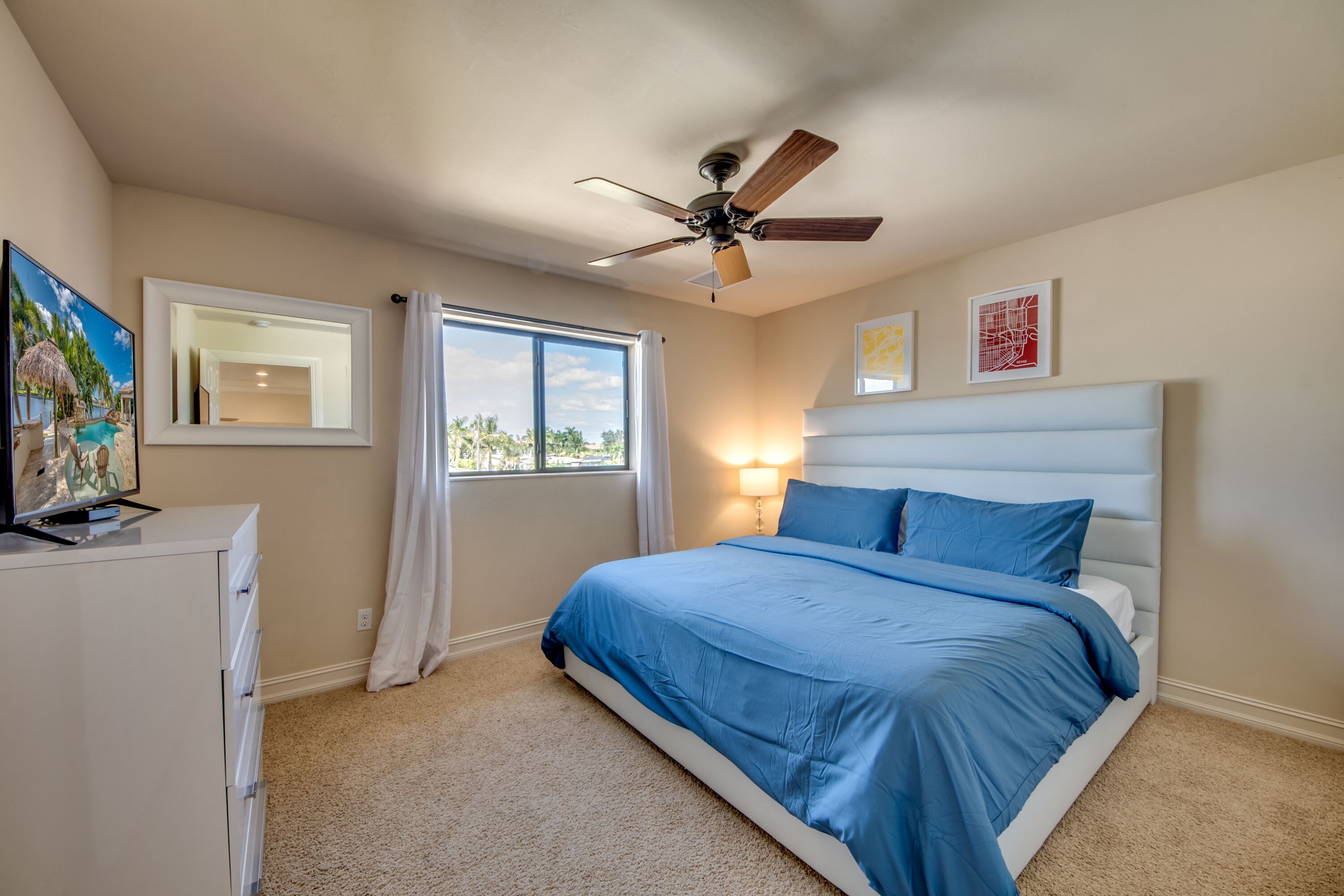 A bedroom with a bed, a ceiling fan, a window, a dresser, and wall art.