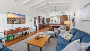 A spacious living room with a wooden coffee table, a blue sofa with patterned cushions, and a large painting of a beach scene. - Fincastle - 5 bedroom, Oceanfront (Pawleys Island)