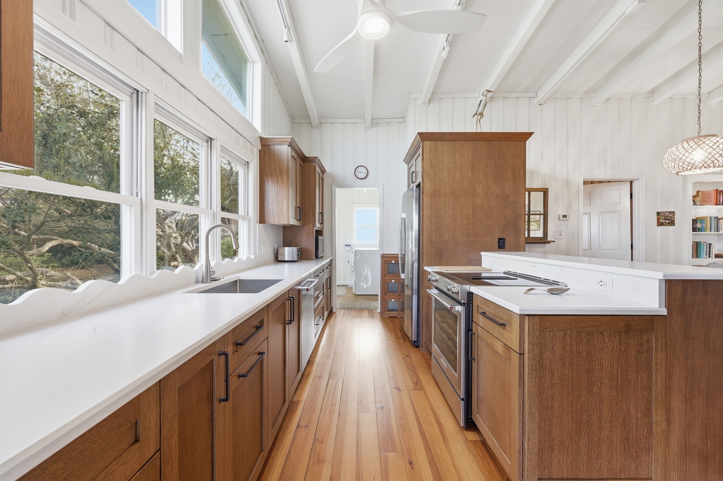 A kitchen with wooden cabinets, a white countertop, and a view of the outdoors.