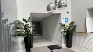 A modern reception area with potted plants, grey sofas, and hanging pendant lights.