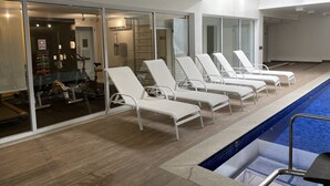 A poolside area with white lounge chairs, a pool, and a gym visible through glass doors.