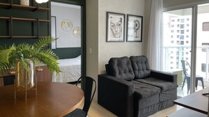 A modern living room with a sofa, a dining table with chairs, a potted plant, and artwork on the walls.