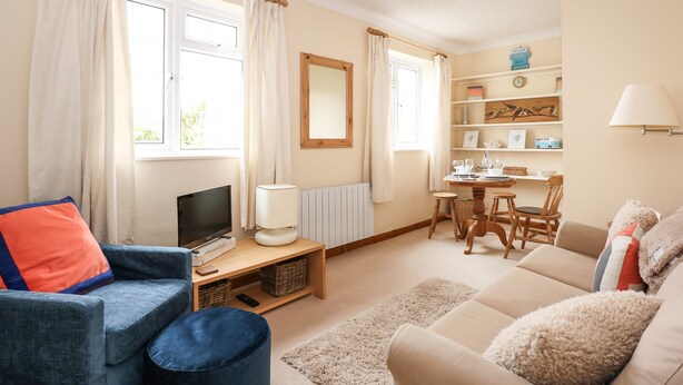 A living room with a sofa, a blue armchair, a TV, a table with chairs, and a bookshelf. - 16 Norfolk Heights (King's Lynn)