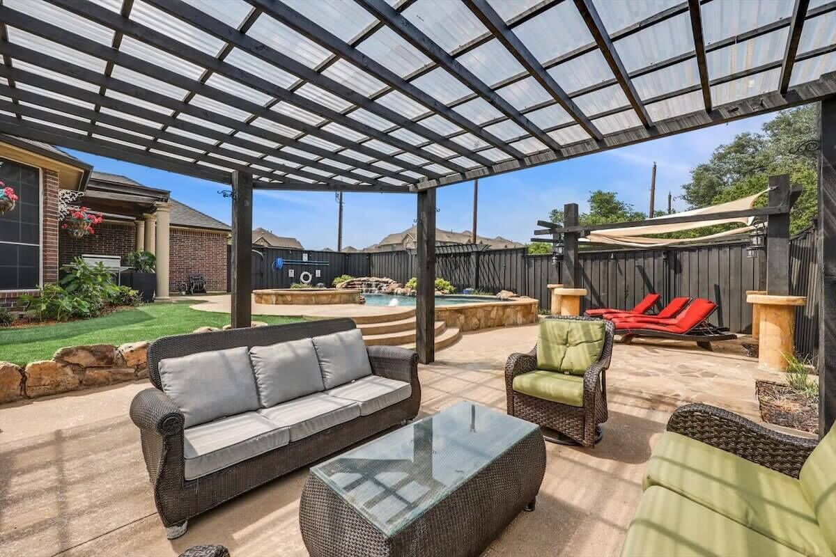 Un patio couvert avec mobilier d’extérieur, une piscine et un jardin clôturé.