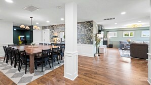 A spacious living area with a wooden dining table surrounded by chairs, a sofa, and a coffee table. - Spacious Home for 12 Near Ark - w/Pool & Hot Tub! (Williamstown)
