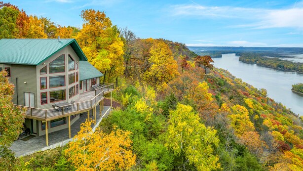 A modern house with a deck overlooking a river, surrounded by autumn foliage.