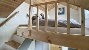 A loft bedroom with a wooden staircase, a bed, and a painting on the wall. - Ashmere Tiny House . Adults Only (Coldingham, Eyemouth)