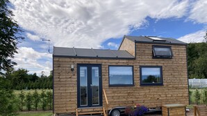 A small wooden house with a sliding door, a patio with a table and chairs, and a garden area. - Ashmere Tiny House . Adults Only (Coldingham, Eyemouth)