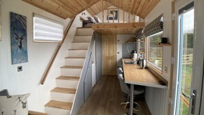 A compact kitchen with a wooden staircase, a dining area with bar stools, and a view through a large window. - Ashmere Tiny House . Adults Only (Coldingham, Eyemouth)