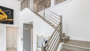 Uma escadaria moderna com guarda-corpo de vidro, design minimalista e uma grande pintura abstrata acima.