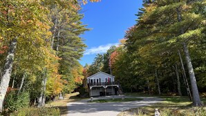 A two-story building with a garage, surrounded by trees with autumn foliage, under a clear blue sky.