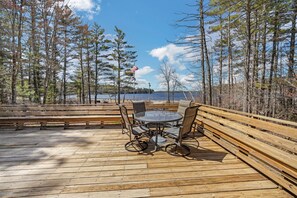 A wooden deck with a round table and chairs, overlooking a body of water and surrounded by trees. - 20 Mile Bay - Tuftonboro - Lake View Pet friendly $50 Fee - Limit 1 (Mirror Lake)