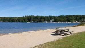 A sandy beach with a picnic table and a lake in the background.