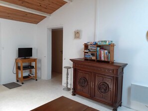 A room with a wooden TV stand, a cabinet with books, and a door leading to another room. - LE CLOS DE DOMINO (Saint-Georges-d'Oléron)