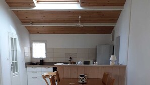 A modern kitchen with wooden beams, a dining table with chairs, and a sofa. - LE CLOS DE DOMINO (Saint-Georges-d'Oléron)