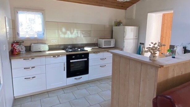 A compact kitchen with white cabinets, a microwave, a stove, and a wooden ceiling. - LE CLOS DE DOMINO (Saint-Georges-d'Oléron)