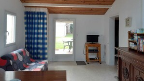A room with a wooden ceiling, a sofa, a television on a wooden stand, and a bookshelf. - LE CLOS DE DOMINO (Saint-Georges-d'Oléron)