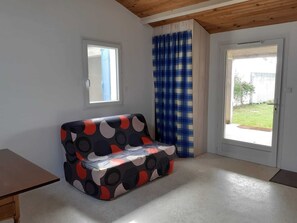 A room with a sofa, a window, and a door leading outside. - LE CLOS DE DOMINO (Saint-Georges-d'Oléron)