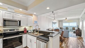 A modern kitchen with stainless steel appliances, a dishwasher, and a large island with a sink. - Crystal Shores 702 by Liquid Life (Gulf Shores)