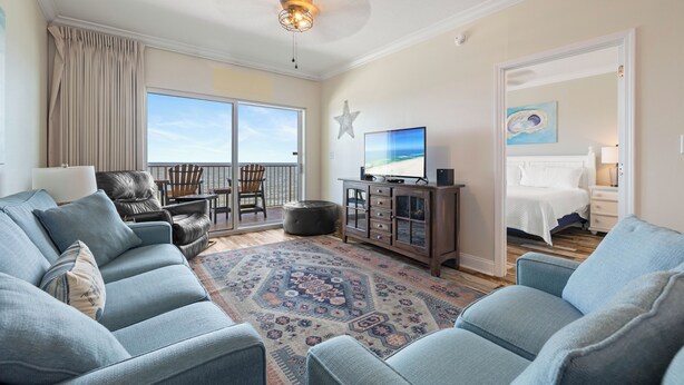 A spacious living room with a large sofa set, a television, and a decorative star on the wall. - Crystal Shores 702 by Liquid Life (Gulf Shores)