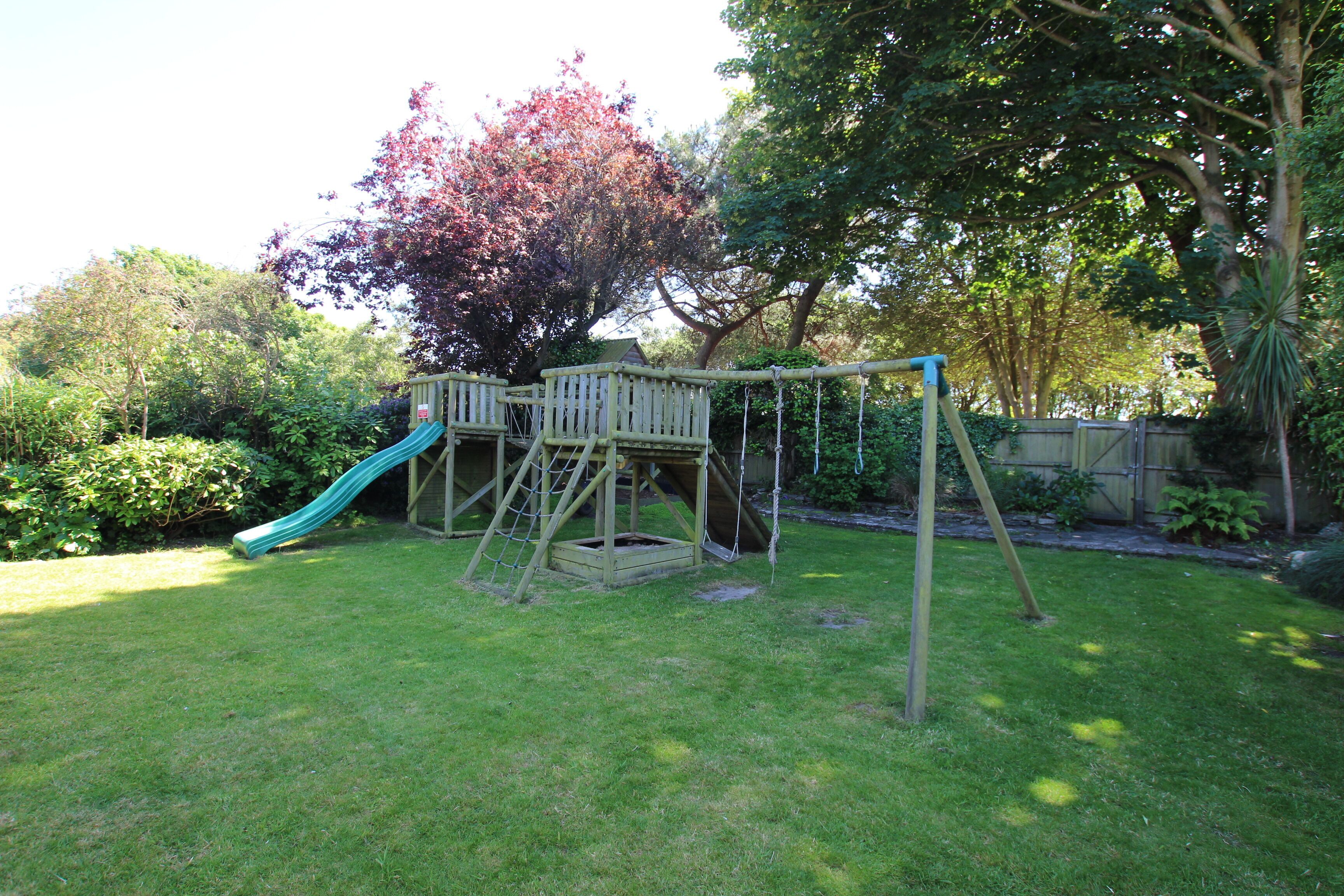 A wooden play structure with a slide in a grassy backyard.