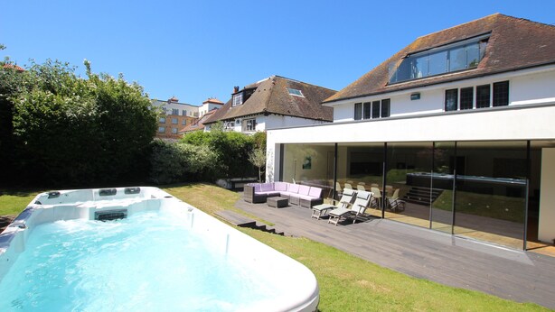 Ein modernes Haus mit Swimmingpool, Außenmöbeln und einer verglasten Terrasse.