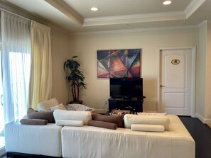 A living room with a sofa, a television, a painting, and a door. - Laguna Bay 302n 3 Bedroom Condo by RedAwning (South Padre Island)