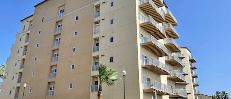 Un hotel de varios pisos con balcones, una zona de estacionamiento y cielo despejado.