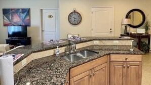 A kitchen with granite countertops, wooden cabinets, a stainless steel sink, and a wall clock.