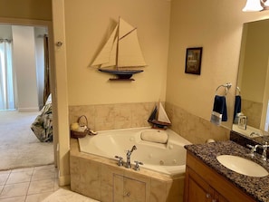A bathroom with a large bathtub, a sink, and a mirror. There is a sailboat decoration on the wall and a towel rack with towels. - Laguna Bay 302n 3 Bedroom Condo by RedAwning (South Padre Island)