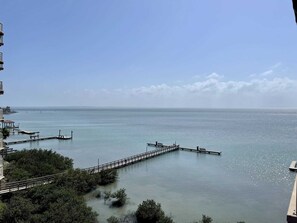 A waterfront view with a pier extending into calm water, surrounded by greenery and buildings. - Laguna Bay 302n 3 Bedroom Condo by RedAwning (South Padre Island)