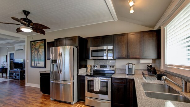 A modern kitchen with stainless steel appliances, dark wooden cabinets, and a granite countertop. - Makani Ea Home 2 Bedroom Home by RedAwning (Hakalau)