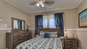 A bedroom with a bed, wooden dresser, nightstand, and a ceiling fan. - Makani Ea Home 2 Bedroom Home by RedAwning (Hakalau)