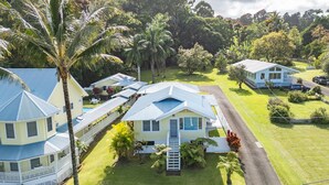 A coastal house with a blue roof, surrounded by lush greenery and palm trees. - Makani Ea Home 2 Bedroom Home by RedAwning (Hakalau)