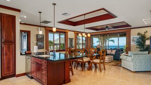 A spacious kitchen with a large island, wooden cabinetry, and a dining area with chairs and a sofa. - Summer Deal Luxury Mauna Kea 3BR Condo with Ocean and Golf Views (Kamuela)