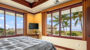 A bedroom with a large bed, a television, and a view of palm trees and a golf course. - Summer Deal Luxury Mauna Kea 3BR Condo with Ocean and Golf Views (Kamuela)