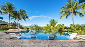 A swimming pool with lounge chairs, palm trees, and a clear blue sky. - Summer Deal Luxury Mauna Kea 3BR Condo with Ocean and Golf Views (Kamuela)